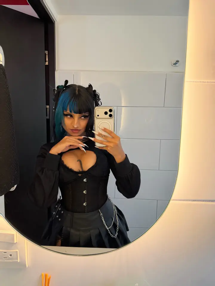 Vesper taking a mirror selfie in a black corset top